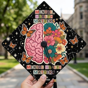 May include: Black graduation cap decorated with a colorful design. The design includes a pink brain, flowers, butterflies, and the text "MENTAL HEALTH MATTERS" in various colors. The tassel is black.