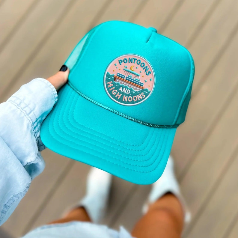 Turquoise cap with a decorative patch held by a person against a neutral background
