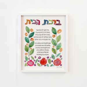 May include: A framed watercolor print featuring Hebrew text and English translation. The artwork includes colorful illustrations of leaves, pomegranates, and decorative elements. The text conveys a message of peace and blessings for a home.