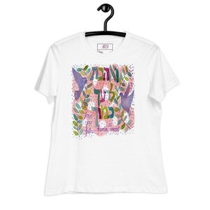 Könnte beinhalten: Ein weißes Kurzarm-T-Shirt mit einer zentralen Grafik aus zwei violetten Vögeln, grünen Blattzweigen und einem rosa gesprenkelten Hintergrund. Das Design enthält hebräischen Text und den englischen Satz, Love your fellow human as yourself.