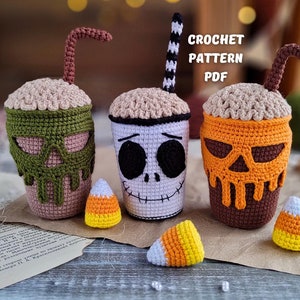 May include: Three crocheted Halloween-themed coffee cups with candy corn. The cups are decorated with a skull, a pumpkin, and a green skull. The text "CROCHET PATTERN PDF" is visible in the image.