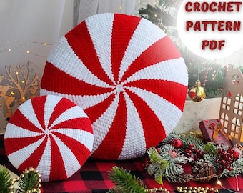 Pode incluir: Dois travesseiros de crochê em forma de bala de menta, um grande e um pequeno, com listras vermelhas e brancas. Os travesseiros estão sobre um tecido xadrez vermelho e preto com uma árvore de Natal e outras decorações no fundo. O texto "CROCHET PATTERN PDF" é visível na imagem.