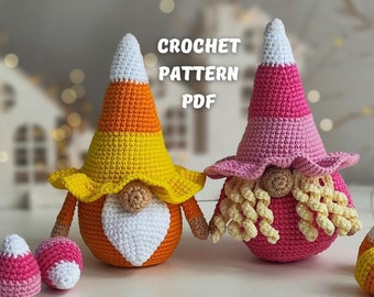 May include: Two crocheted candy corn gnomes, one in pink and white and one in orange, yellow, and white.  The gnomes are sitting on a white surface with two smaller candy corn gnomes in front of them.  The text "CROCHET PATTERN PDF" is visible in the image.