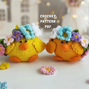 Könnte beinhalten: Zwei gehäkelte gelbe Küken mit Blumenkränzen. Die Küken tragen Kränze aus gehäkelten Blumen in den Farben Blau, Rosa, Lila und Grün. Die Küken sitzen auf einer weißen Oberfläche. CROCHET PATTERN PDF.