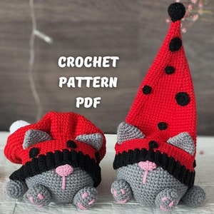 May include: Two crocheted gray cat toys wearing red and black ladybug hats. The hats have black polka dots. The toys are sitting on a white surface with a wooden background. CROCHET PATTERN PDF is written in black text on the background.