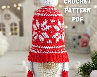 May include: A handmade crochet gnome doll with a red and white patterned hat and matching mittens. The gnome has a white body and a long, beige beard. The text "CROCHET PATTERN PDF" is visible in the image. The scene is decorated with white snowballs and greenery.