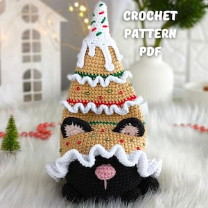 Op de afbeelding: Een gehaakt kerstboom kattenspeeltje in wit, beige, rood en groen. De boom heeft een kattengezicht aan de basis en is versierd met witte glazuur en hagelslag. De tekst "CROCHET PATTERN PDF" is zichtbaar.