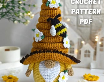 May include: A handmade crochet gnome with a beehive hat, adorned with white flowers and a bee. The gnome has a yellow body, a white beard, and a brown hat brim. The text "CROCHET PATTERN PDF" is visible.