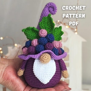 以下が含まれることがあります： 紫色のブドウのノームのアミグルミのクロシェパターンPDF。ノームは白いひげと、紫と青のブドウがついた緑色のブドウのつるで作られた帽子をかぶっています。