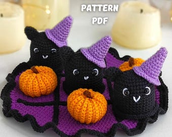Puede incluir: Decoración de Halloween de ganchillo con tres murciélagos negros con sombreros de bruja morados y tres calabazas naranjas. Los murciélagos están colocados sobre una alfombra morada con borde negro. El texto "CROCHET PATTERN PDF" es visible.