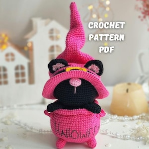 May include: A crocheted black cat wearing a pink witch hat and sitting in a pink cauldron with the word "HALLOWEEN" written on it.