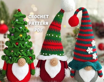 May include: Three crocheted Christmas gnomes, one with a green and red striped hat, one with a red hat, and one with a green Christmas tree hat. The gnomes are sitting on a white surface with a red and green garland in the foreground.