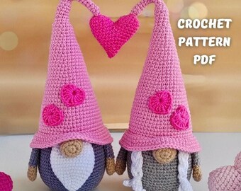 Könnte beinhalten: Zwei rosa gehäkelte Gnome mit Herzen auf ihren Hüten, die ein rosa Herz zwischen sich halten. Die Gnome sitzen auf einer hellbraunen Oberfläche mit rosa Herzen, die um sie herum verstreut sind. CROCHET PATTERN PDF steht in weißer Schrift auf einem schwarzen Rechteck.