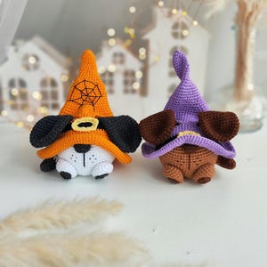May include: Two crocheted Halloween dog toys wearing witch hats. One dog is orange with a black spiderweb on its hat and the other is brown with a purple hat.