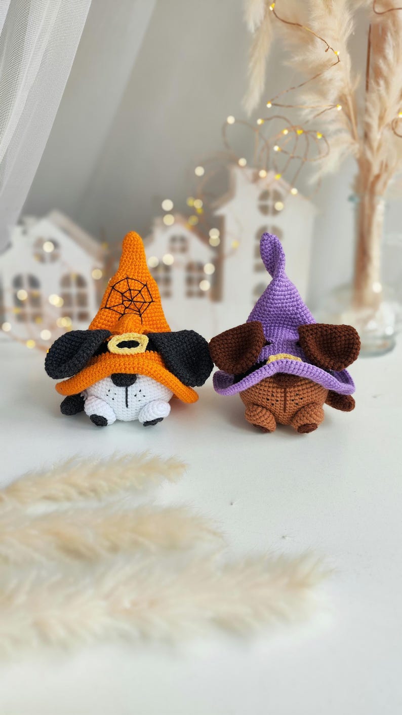 May include: Two crocheted Halloween dog toys wearing witch hats. One dog is orange with a black spiderweb on its hat and the other is brown with a purple hat.