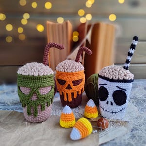 May include: Three crocheted Halloween-themed mugs with candy corn accents. The mugs are decorated with a skull, a pumpkin, and a skeleton face.