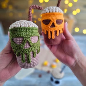 May include: Two crocheted Halloween-themed coffee cups with a skull design. One cup is green and the other is orange.
