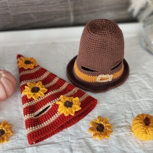 May include: Crocheted Thanksgiving-themed decorations. Includes a brown pilgrim hat with a yellow band and buckle, a red and cream striped hat with yellow sunflowers, and additional sunflower and pumpkin accents. The items are handmade.
