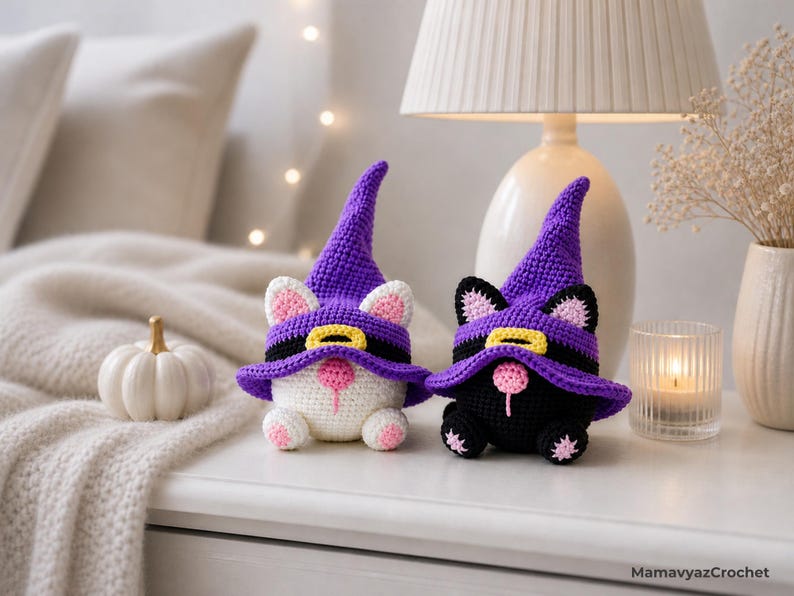 May include: Two crochet cat figurines wearing purple witch hats with black bands and yellow buckles. One cat is white with pink ears and paws, the other is black with pink ears and paws. The cats are Halloween-themed decorations.