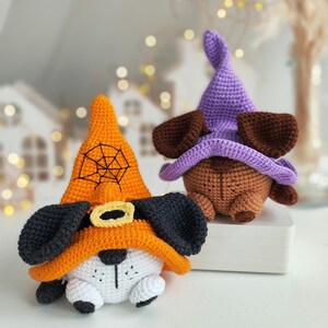 May include: Two crocheted Halloween dog toys. One is orange with a black spiderweb and black ears. The other is brown with purple ears and a purple hat.