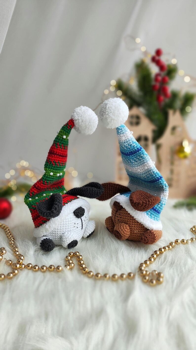 May include: Two crocheted stuffed animals wearing Santa hats. The animal on the left is white with black ears and a black nose. The animal on the right is brown with black ears and a black nose. Both animals are wearing red and green Santa hats with white pom-poms.