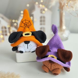 May include: Two crocheted Halloween witch dog toys. One is wearing an orange hat with a black spiderweb and the other is wearing a purple hat.
