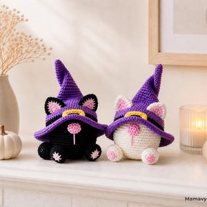 May include: Two crocheted cat figurines, one black and one white, wearing purple witch hats with yellow bands. The cats have pink ears and noses, and are decorated with pink and black accents. The figurines are Halloween-themed.