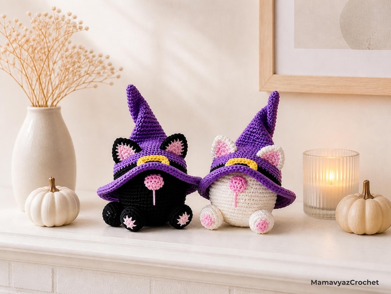 May include: Two crocheted cat figurines, one black and one white, wearing purple witch hats with yellow bands. The cats have pink ears and noses, and are decorated with pink and black accents. The figurines are Halloween-themed.