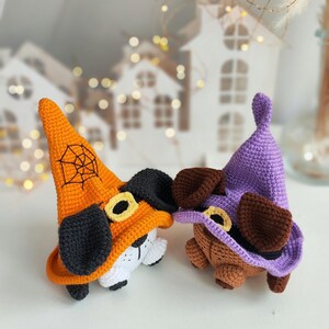 May include: Two crocheted Halloween dog toys wearing witch hats. One hat is orange with a black spiderweb and the other is purple. Both dogs have brown ears and black noses.