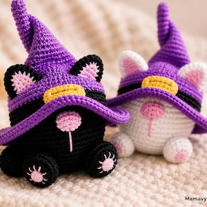 May include: Two handmade crochet cat figures, one black and one white, wearing purple witch hats with yellow bands. The cats have pink ears and noses, and are sitting on a soft, textured surface. The figures are whimsical and decorative.