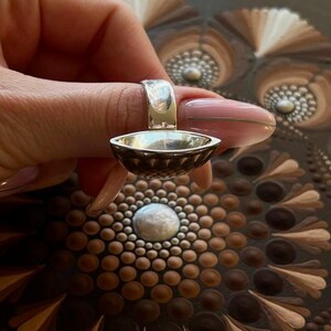Peut inclure: Une bague en argent avec un dessus en forme de bol. La bague est portée sur un doigt et le bol est orienté vers le haut.