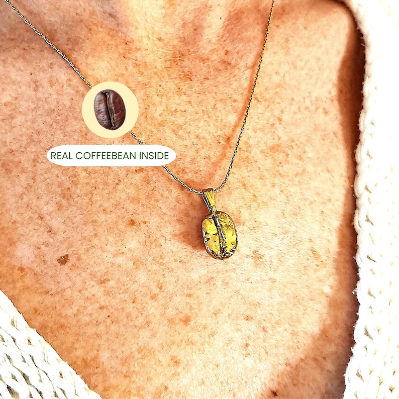 May include: A gold-colored pendant necklace featuring a coffee bean design. The pendant hangs from a delicate silver chain. The image includes the text "REAL COFFEEBEAN INSIDE" next to a graphic of a coffee bean.