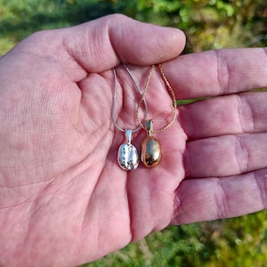 A silver and gold plated coffee bean shown on chain in hand. Made from a real coffee bean which is contained inside the pendant