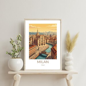 Puede incluir: Lámina artística enmarcada con una ilustración estilizada de Milán, Italia. La obra representa la arquitectura de la ciudad, incluyendo una catedral, edificios y un canal. La impresión tiene un marco beige y el texto "MILAN ITALY" en la parte inferior.