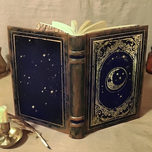 Peut inclure: Un journal relié en cuir bleu foncé avec des accents dorés et un motif de croissant de lune et d'étoiles sur la couverture.