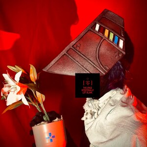 May include: A brown, angular headpiece with colourful accents and a white scarf. A small orange and white pot with a blue cross design holds a plant with white and orange flowers. The text "THIS SPACE INTENTIONALLY LEFT BLANK" is visible.