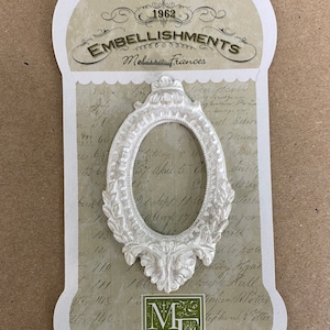 May include: White oval picture frame with ornate details, made by Melissa Frances Embellishments. The frame is on a background of vintage-looking paper with handwritten text.