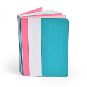 Puede incluir: Un pequeño cuaderno colorido con una cubierta turquesa y una columna vertebral con puntos blancos. El cuaderno tiene páginas rosas, azul claro y blancas.