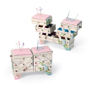 May include: Two vintage-style wooden sewing boxes with pink cushions and multiple drawers. The boxes are decorated with floral patterns and have small legs.