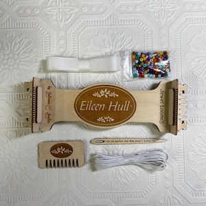 May include: A wooden Jewel Loom kit by Eileen Hull, featuring a wooden loom, a bag of colorful beads, white elastic cord, a wooden comb, and a needle with the quote "It's not perfect, but that doesn't bother me".