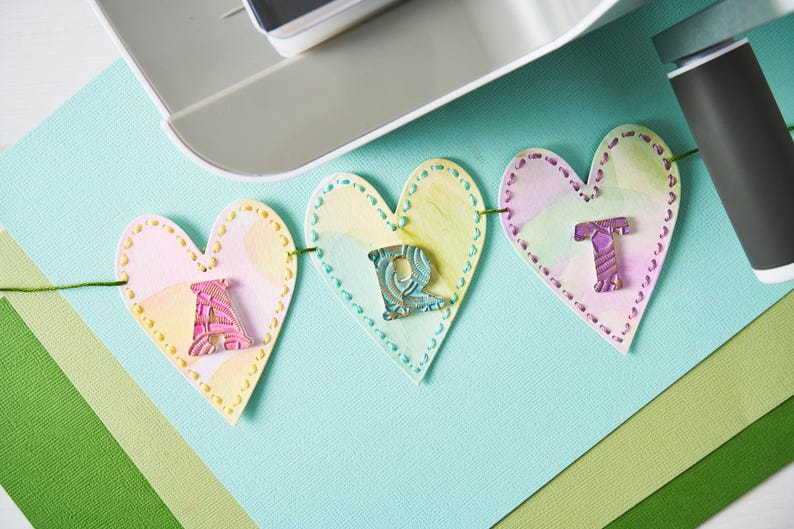Peut inclure: Une guirlande d&eacute;corative avec des pendentifs en forme de c&oelig;ur &eacute;pelant le mot "ART". Chaque pendentif est de couleur pastel avec une bordure cousue et une lettre d&eacute;corative. La guirlande est suspendue &agrave; un fil vert, id&eacute;ale pour un projet cr&eacute;atif.