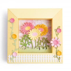 May include: A yellow frame with a white picket fence, green grass, and three yellow, pink, and orange paper flowers with green leaves. The flowers are layered to create a 3D effect.