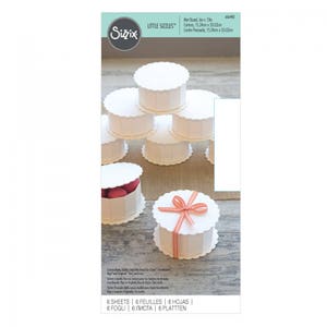 May include: A set of six white scalloped-edge cardboard boxes with lids. The boxes are stacked in a pyramid shape. The box in the front has a red and white gingham ribbon tied around it. The boxes are 6 inches in diameter and 13 inches tall. The text on the packaging reads "Little Sizzles" and "6 Sheets | 6 Feuilles | 6 Hojas | 6 Fogli | 6 Листа | 6 Platten".