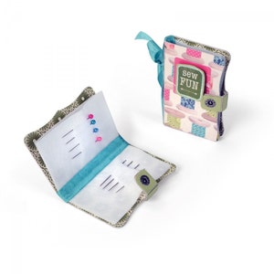 May include: A small green and white fabric sewing kit with a blue ribbon and a button closure. The kit is open and has a white mesh interior with pins and needles. The front of the kit has a colourful pattern of spools of thread and the text "sew fun".
