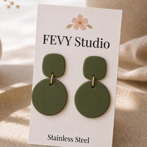 May include: A pair of olive green earrings on a white display card labeled FEVY STUDIO and Stainless Steel. Each earring features a small square top piece connected by a gold-toned metal ring to a larger circular bottom piece with a matte finish.