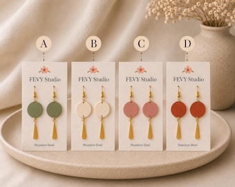 May include: Four pairs of dangle earrings on white display cards labelled A, B, C, and D. Each pair features a circular disc in sage green, cream, dusty rose, or terracotta, paired with a gold-toned metal drop and stainless steel hooks.