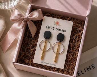 以下が含まれることがあります： FEVY Studio Handmade Earringsと書かれた台紙にセットされたピアス。黒い丸みを帯びた四角いトップ、シルバーのフープ、ゴールドの縦型バーで構成され、サテンリボン付きの淡いピンクのギフトボックスに入っています。