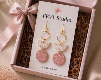 以下が含まれることがあります： FEVY StudioおよびStainless Steelと記載された白い台紙にセットされたドロップピアス。ゴールドのフープ、質感のあるクリーム色の半円、質感のあるダスティピンクの円で構成され、ピンクのギフトボックスに入っています。