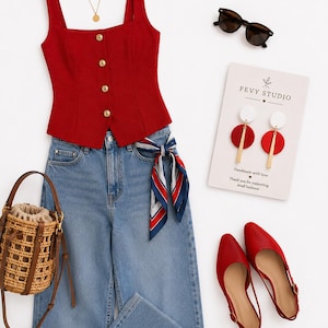 Puede incluir: Un top rojo sin mangas con botones dorados, vaqueros azules con un pa&ntilde;uelo rojo, blanco y azul, un bolso tipo cubo de paja trenzada, zapatos rojos destalonados, gafas negras, un collar dorado y pendientes circulares en una tarjeta Fevy Studio.