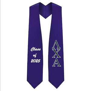 May include: A purple graduation stole with white text reading "Class of 2025" and green Greek letters. The stole is made of a smooth fabric and is designed to be worn over the shoulders.
